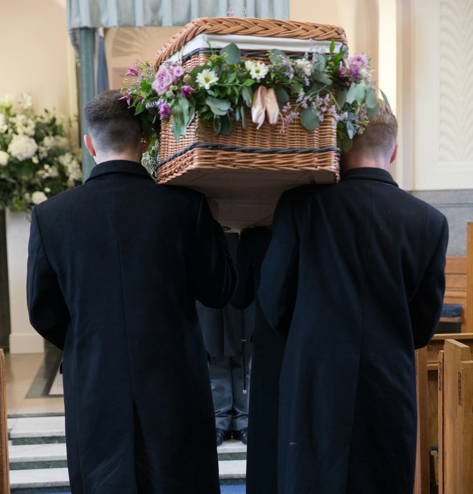 A Group Of Men And Women Dressed In Black Carrying A Willow Coffin On Their Shoulders